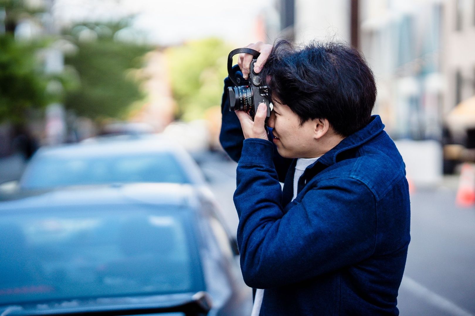 Gatufotograf fotograferar på en stadsgata bland parkerade bilar